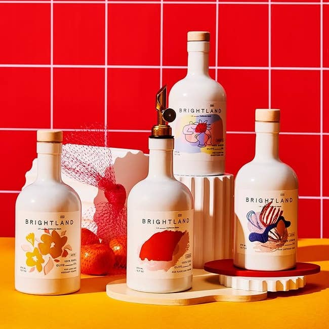 Four Brightland olive oil bottles with artistic labels are displayed on a vibrant set, featuring abstract designs that highlight gourmet shopping choices