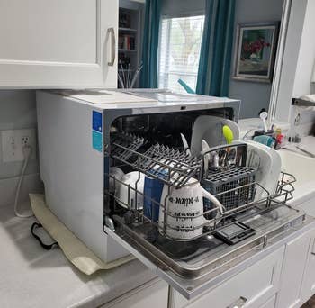 reviewer photo of the open dishwasher on a kitchen counter holding various mugs, plates, and utensils