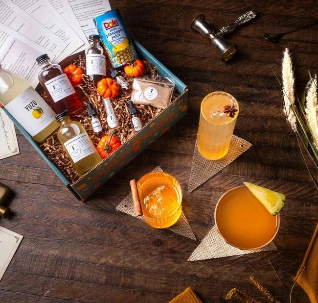 a cocktail kit filled with mixers and mini pumpkins, surrounded by drink glasses and cocktail accessories