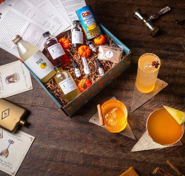 a cocktail kit filled with mixers and mini pumpkins, surrounded by drink glasses and cocktail accessories