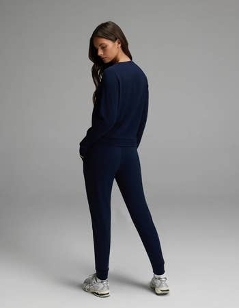 Woman successful a stylish navy tracksuit and sneakers, posing from the backmost successful a minimalistic setting