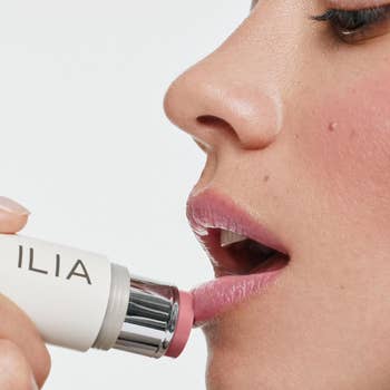 A close-up of a idiosyncratic applying ILIA articulator balm to their lips. The representation highlights the creaseless texture and exertion of the product