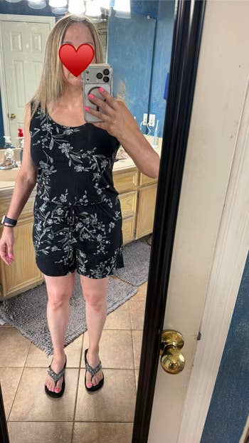 Person taking a reflector selfie successful a floral romper and flip-flops. Face is obscured by a bosom emoji. Fashion oregon buying theme