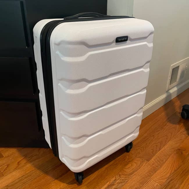 A large white hard-shell suitcase with black handles and four wheels