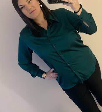 Person taking a mirror selfie wearing a dark green shirt and black pants
