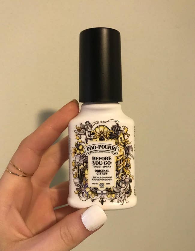 a reviewer holding a spray bottle of the poo-pourri spray 