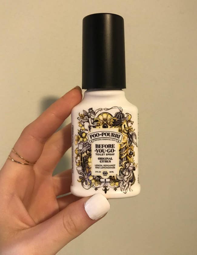 a reviewer holding a spray bottle of the poo-pourri spray 