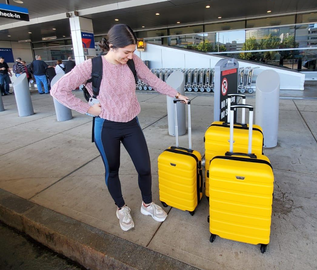 a reviewer with three hard shell yellow suitcases in varying sizes