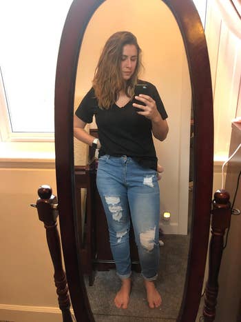 A reviewer in front of an oval mirror, wearing a black t-shirt and ripped jeans, taking a mirror selfie