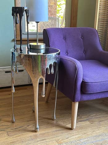reviewer image of the silver aluminum drip end table next to a purple armchair