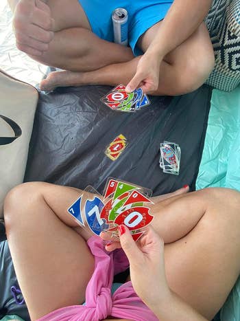 Two people playing UNO on a portable surface, with cards in hand and a discard pile in view
