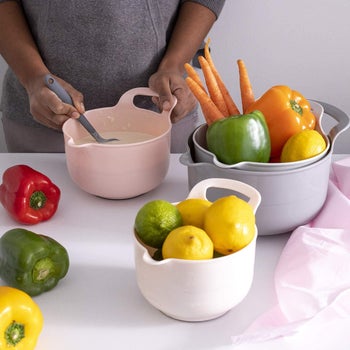 four different sized bowls with handles and spouts in light pink to grey