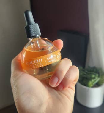 Reviewer holding a bottle of Cuccio cuticle oil against a blurred background