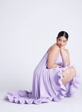 Person successful  stylish, flowing gown poses gracefully, kneeling connected  1  knee, looking off-camera. Fashion-forward look   with elegant ruffled detailing