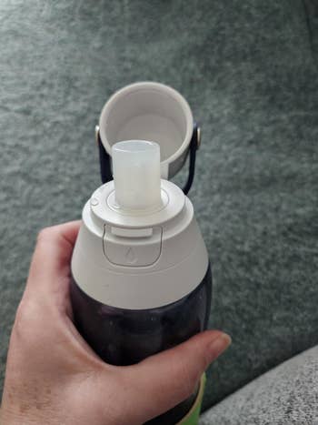 A reviewer holding a reusable water bottle with a flip-top cap and a pop-up straw