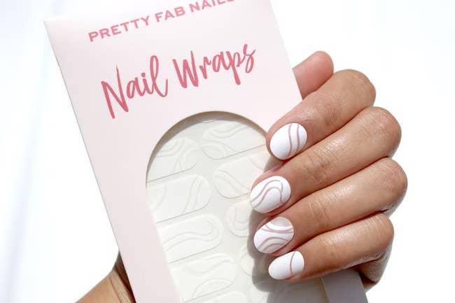 a model wearing the white and negative space nail wraps while holding a pack of the wraps 