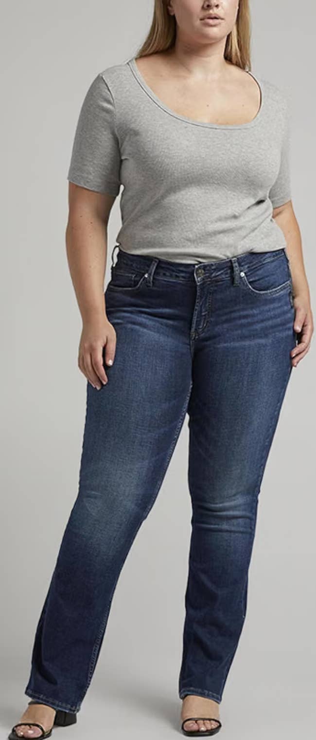 Person wearing a fitted grey  top, acheronian  jeans, and sandals, lasting  successful  a neutral pose