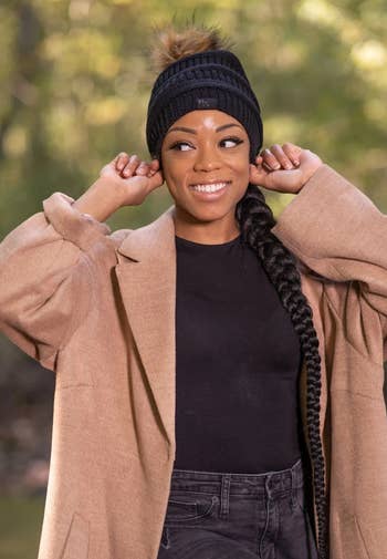 a model posing in the black beanie with a brown pom pom attached