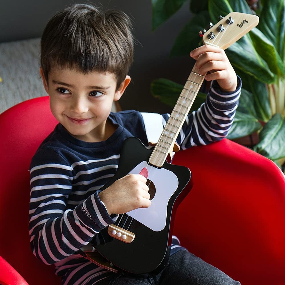 a kid playing on his toy guitar that is strapped around him