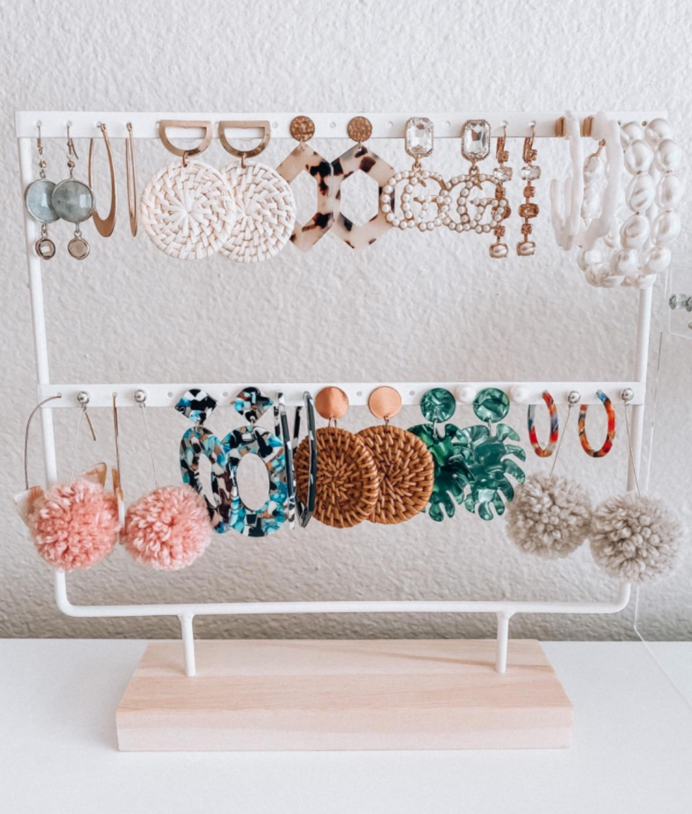 White two tiered earring stand with wooden base holding hoop and drop earrings 