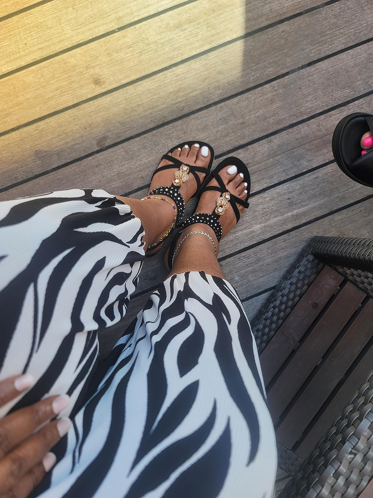 Person wearing zebra-patterned pants and stylish achromatic  sandals with metallic embellishments, seated connected  a wood   deck