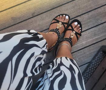 Person wearing zebra-patterned pants and stylish achromatic sandals with metallic embellishments, seated connected a wood deck