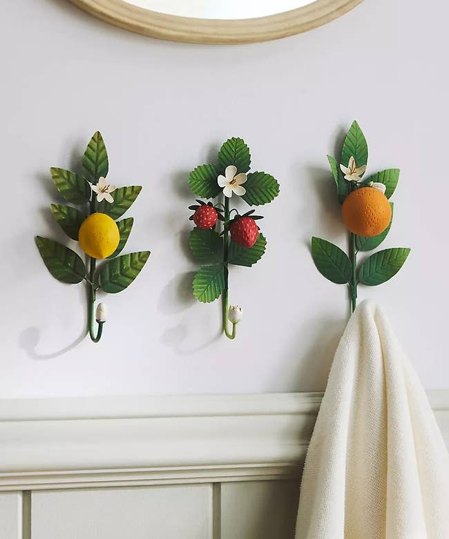 Three decorative partition hooks shaped similar fruit-bearing branches with lemons, strawberries, and oranges, holding a light-colored towel