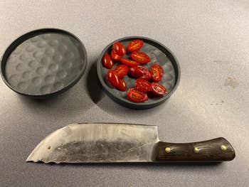 A chef's knife beside a bowl with sliced cherry tomatoes on a countertop