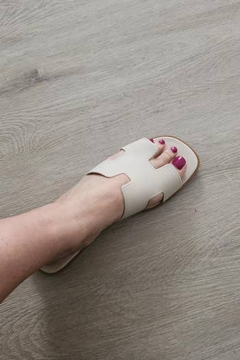 A foot wearing a white open-toe beige sandal 