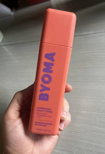 Person holding a BYOMA Hydrating Milky Toner, which includes obstruction  lipids, glycerin, and oatmeal extract