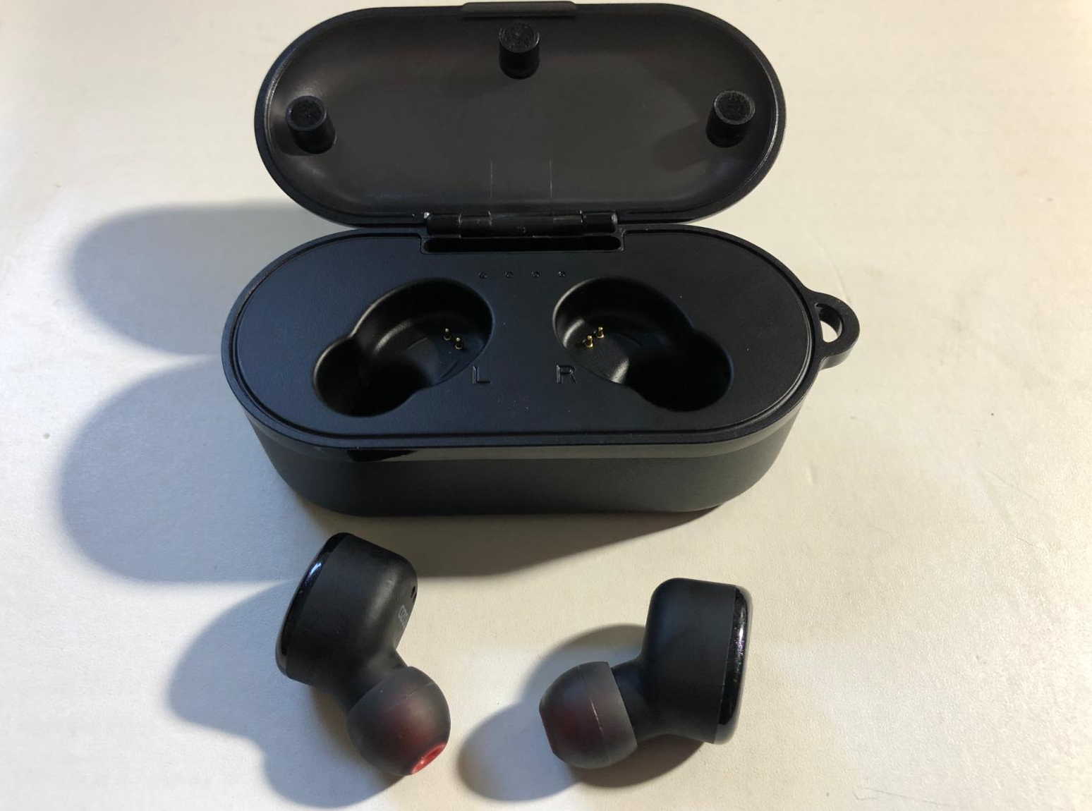 a reviewer photo of the earbuds next to the included charging/storage case 