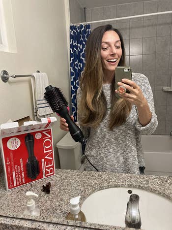 reviewer holds same hot-air brush after drying wavy brown hair