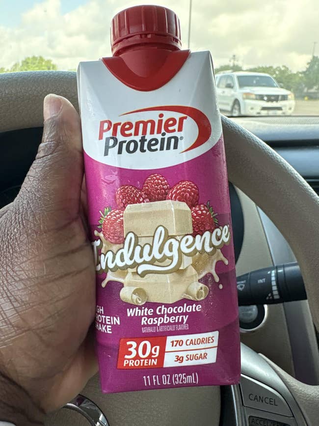 Hand holding a carton of Premier Protein Indulgence shake, White Chocolate Raspberry flavor, highlighting 30g protein, 170 calories, 3g sugar