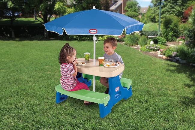 two children sitting at a little tikes picnic table with an umbrella