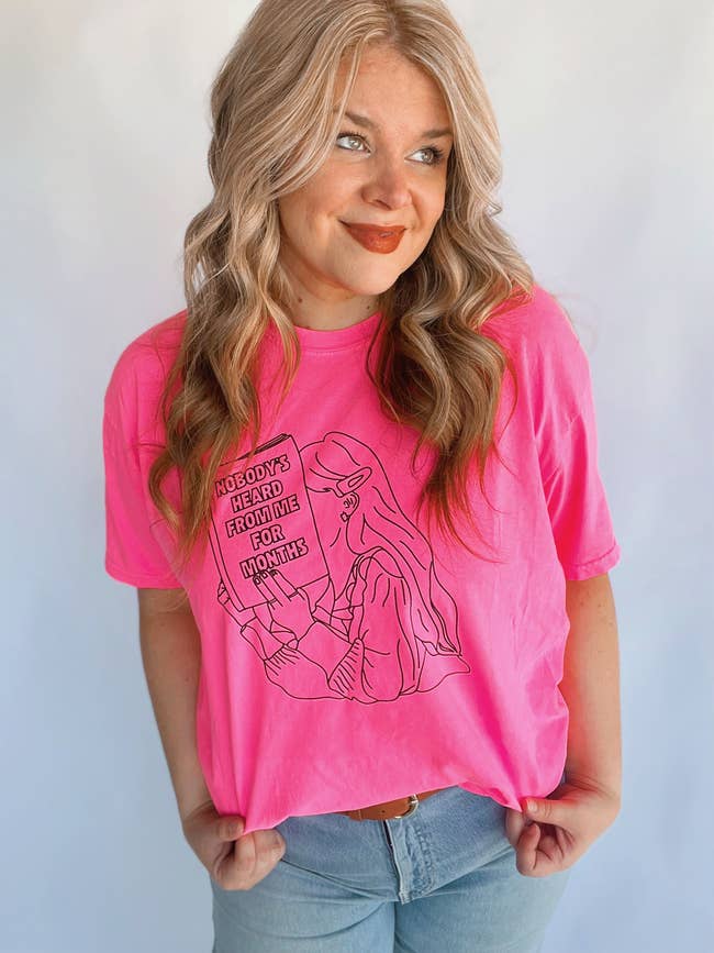 a hot pink t-shirt with an illustration of a girl on it reading a book that says 