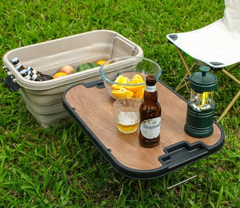 Folding camping box with table feature, drinks and fruit on top, set on grass. Text highlights joy of outdoor camping