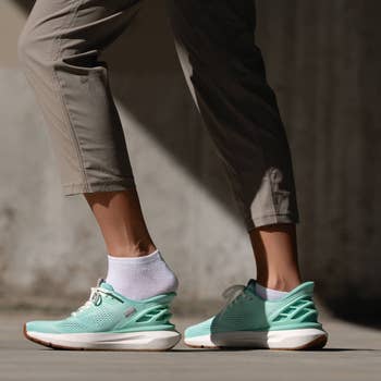 Person wearing beige pants, achromatic  socks, and stylish teal sneakers with a unsocial   bottommost   design, walking outdoors