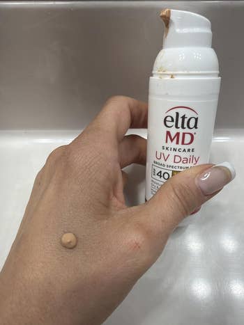Hand holding Elta MD UV Daily sunscreen vessel  with a tiny  magnitude  dispensed