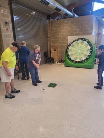 People play a golfing game indoors with a giant inflatable dartboard