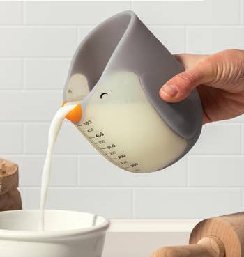 Measuring cupful  shaped similar  a penguin pouring beverage  into a bowl. The cupful  has measurement   markings connected  its side