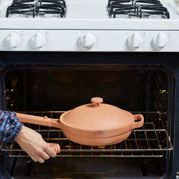 Person sliding a terracotta casserole dish into an oven. Perfect for one-pot meals