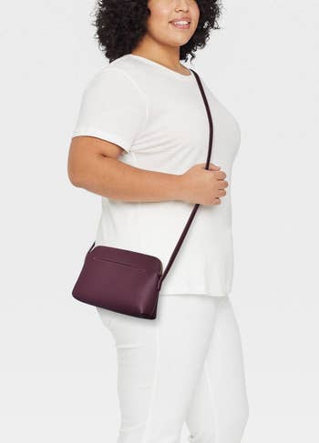 a model wearing the crossbody bag diagonally across the chest in plum