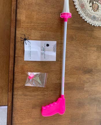 reviewer photo of the pink critter catcher on a table next to some small items it came with and a fake spider
