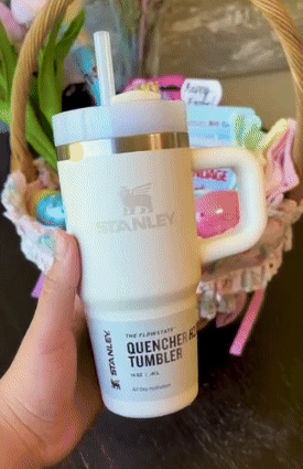 Person holding a Stanley Quencher H2.0 Tumbler, fashionable  for hydration, successful  beforehand   of an Easter handbasket  with colorful items