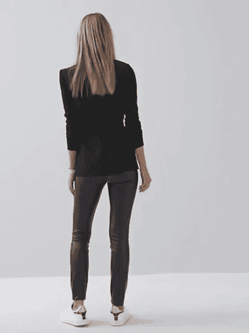 Video of model showing front and back view of smooth black faux leather leggings with white sneakers and black tie-front cardigan