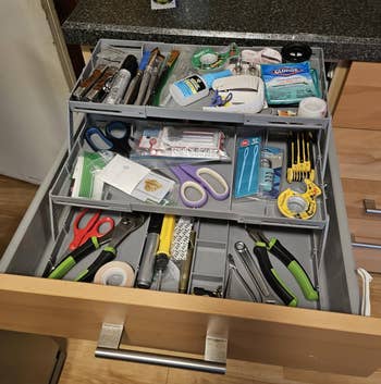 Entertainmment news A drawer filled with various tools and supplies including scissors, tape, markers, batteries, glue sticks, a ruler, and other miscellaneous household items