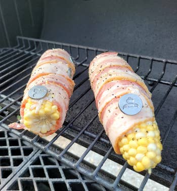 the bacon holders keeping bacon wrapped around two ears of corn on a grill