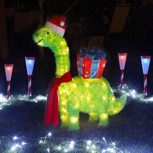 a dinosaur wearing a santa hat, scarf, and carrying a present on its back