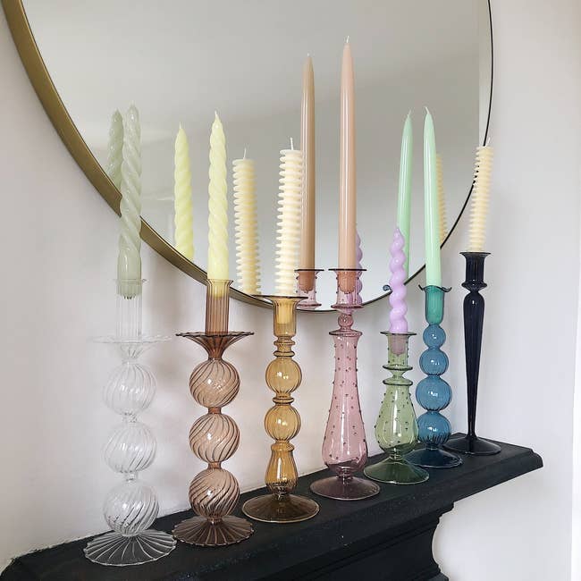 An assortment of decorative candles with unique textures on stylized holders, displayed on a mantelpiece next to a round mirror