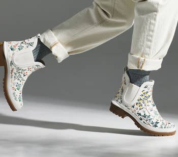 a model in white rain booties with a floral pattern on them